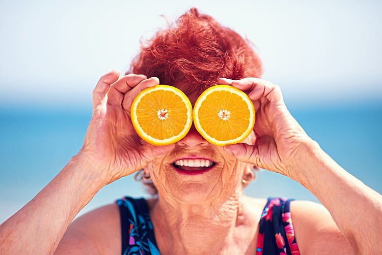 Ältere Frau hält sich zwei Orangenhälften vor die Augen.