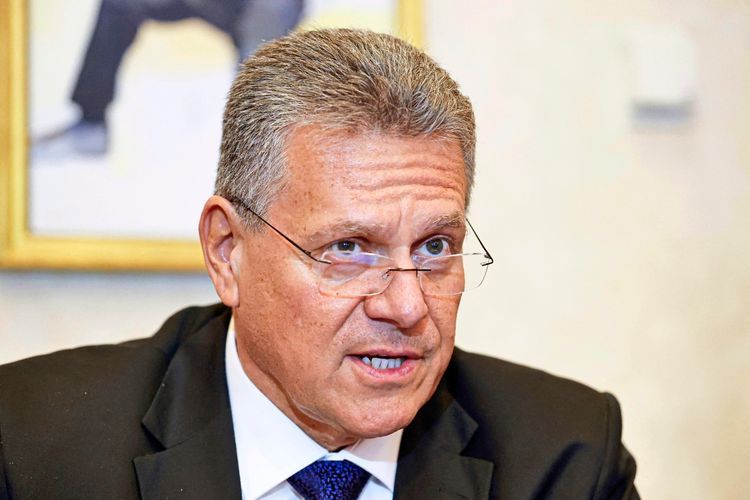 Ein Mann mittleren Alters mit grauem Haar trägt eine Brille und einen dunklen Anzug mit weißem Hemd und Krawatte. Er spricht und wirkt engagiert. Der Hintergrund ist unscharf.
