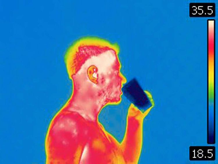 Infrarotkamera-Aufnahme eines Mannes mit freiem Oberkörper, dessen Körperoberfläche rot-weiß erscheint und damit warm. Er trinkt aus einem kalten und daher dunkelblau sichtbaren Glas.