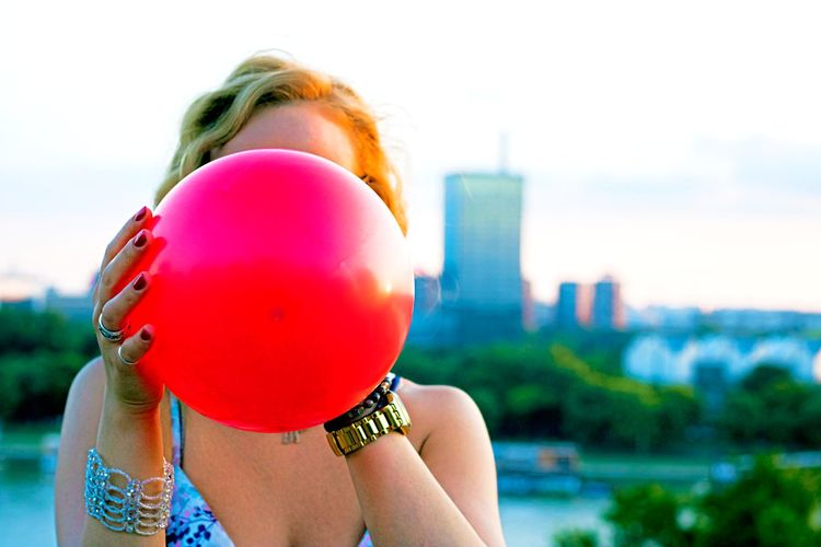 Junge Frau hält einen roten Luftballon vor dem Gesicht.