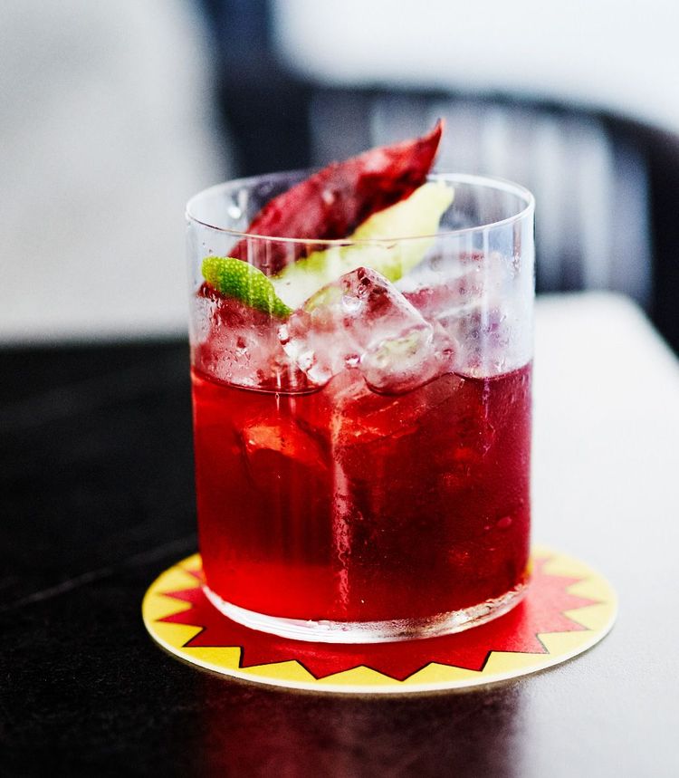 Ein Glas mit roter Flüssigkeit, Eiswüfel und einer Limettenzeste.