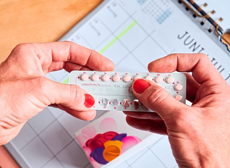 Über einem Kalender nimmt sich eine Frau die nächste Pille aus einer Monatspackung der Antibabypille.
