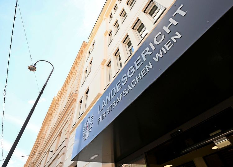 Außenansicht des Eingangsbereichs des Landesgerichts für Strafsachen in Wien, aufgenommen an einem sonnigen Tag, mit leicht bewölktem Himmel im Hintergrund.