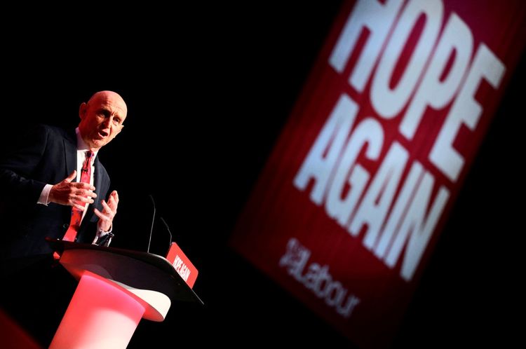 Ein Mann spricht auf einer Bühne während einer Veranstaltung der Labour Party. Im Hintergrund ist ein rotes Banner mit der Aufschrift 