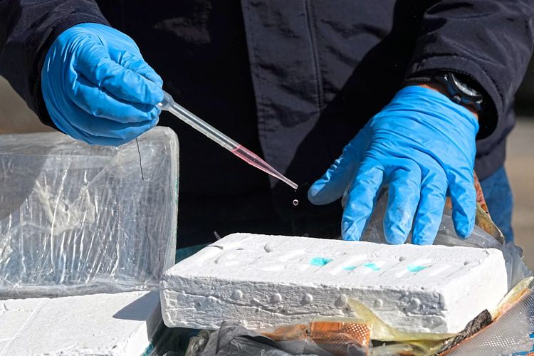Eine Person testest mit einer Flüssigkeit aus einer Pipette den Reinheitsgehalt eines Kokainblocks.