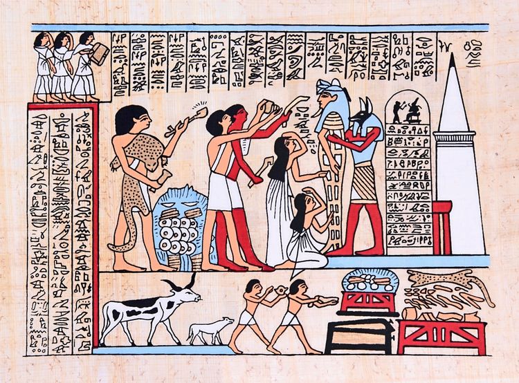 Ägyptische Hieroglyphen-Darstellung auf Papyrus: Die Szene zeigt mehrere Figuren in typischer ägyptischer Kleidung und Götterdarstellungen, darunter eine Figur mit einem Schakalkopf. Menschen stehen kniend und tragen Opfergaben dar. Daneben befinden sich Tiere, darunter eine Kuh, sowie weitere Opfergaben. Über und neben der Szene sind Hieroglyphentexte dargestellt.
