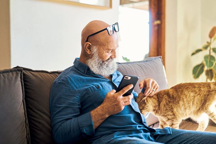 Ein älterer Mann streichelt eine Katze, ist ihr zugewandt und wirkt, als würde er mit ihr sprechen