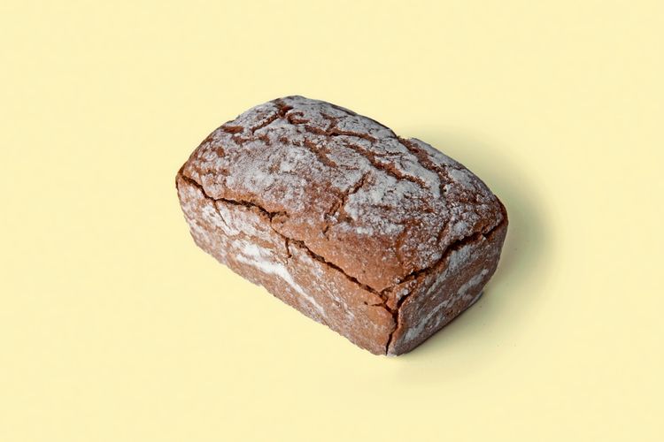 Ein Laib Roggenbrot mit leicht bemehlter Kruste, auf einem hellgelben Hintergrund platziert.