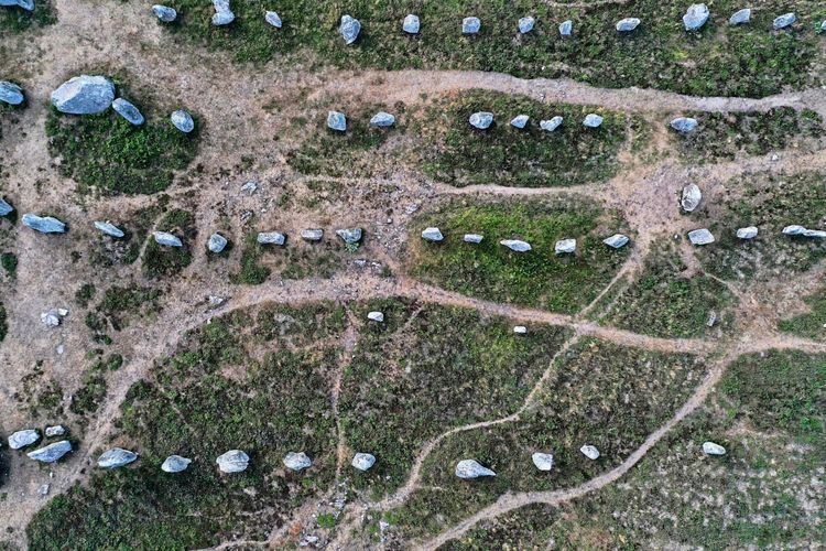 Luftaufnahme der Carnac-Steine, einer Ansammlung von neolithischen stehenden Steinen in Carnac, Westfrankreich. Die Steine sind in Reihen auf einem gras- und erdigen Gelände angeordnet, umgeben von Wegen und Vegetation.