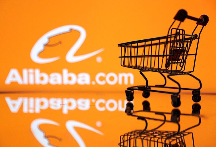In dieser Illustration ist ein Einkaufswagen vor dem Alibaba-Logo zu sehen.