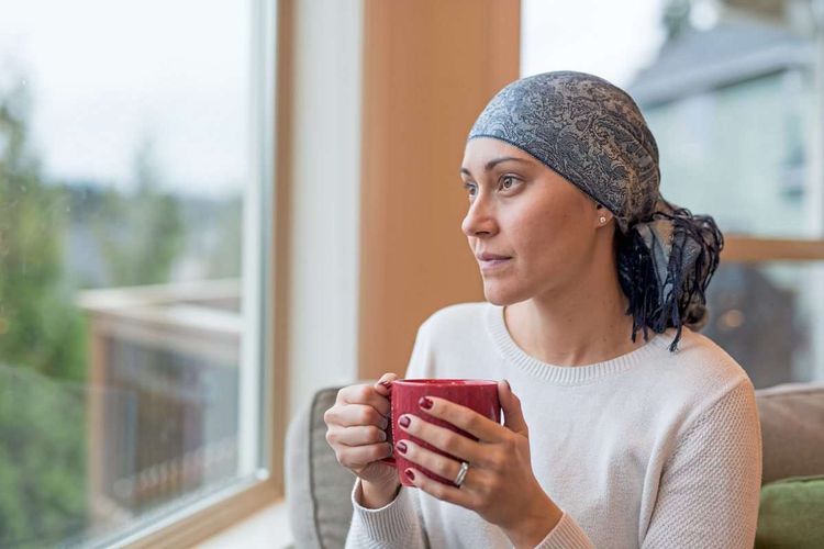 Krebsüberlebende mit Kopftuch schaut aus dem Fenster
