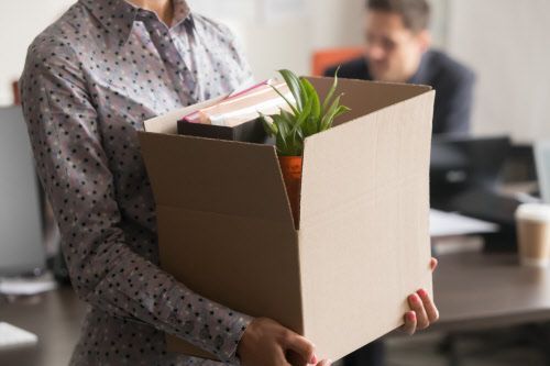 Eine Büroarbeiterin verlässt mit Kartonbox den Arbeitsplatz
