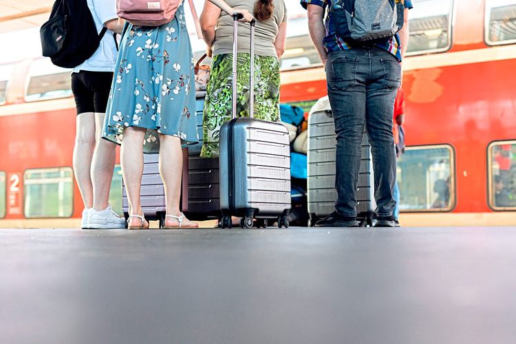 Eine Gruppe Reisender steht mit Koffern am Bahnsteig vor einem Zug