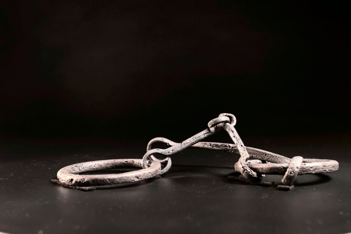 Römische Eisenfessel mit zwei ringförmigen Enden, vermutlich ein archäologischer Fund, auf schwarzem Hintergrund präsentiert.