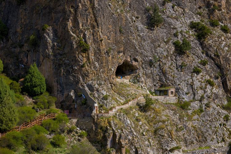 Foto der Höhle in einem steilen Berg, heute kommt man über Brücken und Stiegen in die Nähe des Eingangs, an dem ein kleines Häuschen steht.
