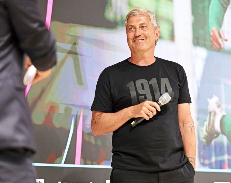 Ein Mann mit grauen Haaren trägt ein schwarzes T-Shirt mit der Aufschrift 