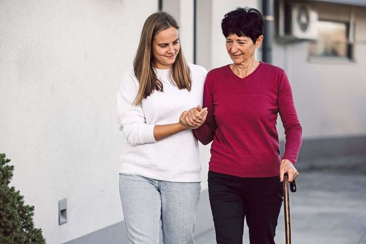 Pflegerin hilft älterer Frau beim Gehen.