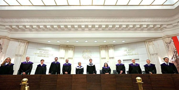 Verfassungsrichterinnen und Verfassungsrichter stehen in einer Reihe im Verhandlungssaal am Verfassungsgerichtshof.