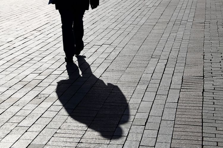 Ein Mann läuft auf einer gepflasterten Straße, wobei sein Schatten deutlich auf dem Boden sichtbar ist.