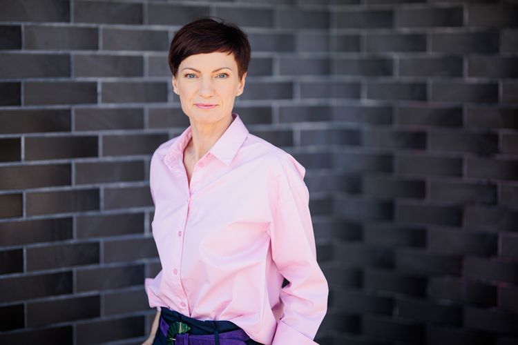 TV-Chefin Monika Garbačiauskaitė-Budrienė in einem rosa Hemd vor einer geschwungenen Mauer