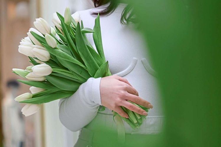 Zoom auf einen Strauß weißer Tulpen in der Hand einer Frau