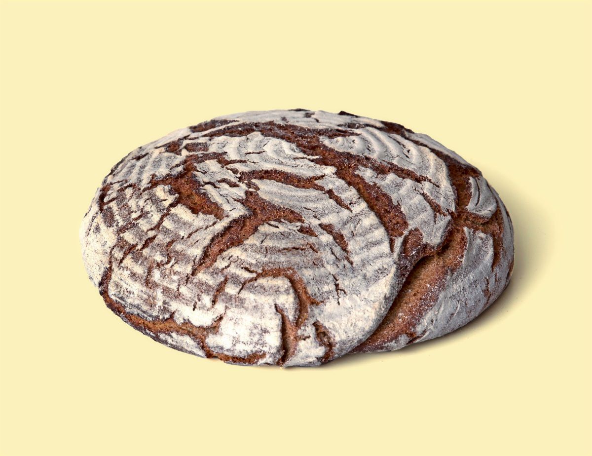 Ein rustikales Roggenbrot mit einer knusprigen, bemehlten Kruste, vor einem hellgelben Hintergrund.
