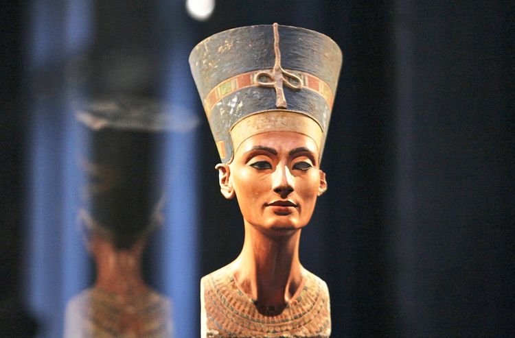Profilansicht der berühmten Büste der Nofretete, ausgestellt im Nordkuppelsaal des Neuen Museums auf der Berliner Museumsinsel. Die Büste zeigt fein ausgearbeitete Details wie das königliche Kopftuch und den eleganten Hals. Im Hintergrund ist ein dunkler, unscharfer Bereich erkennbar.