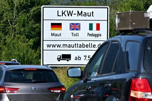 Zwei Autos stehen auf einer Autobahn vor einem Verkehrsschild, das auf die Lkw-Maut in Österreich aufmerksam macht.