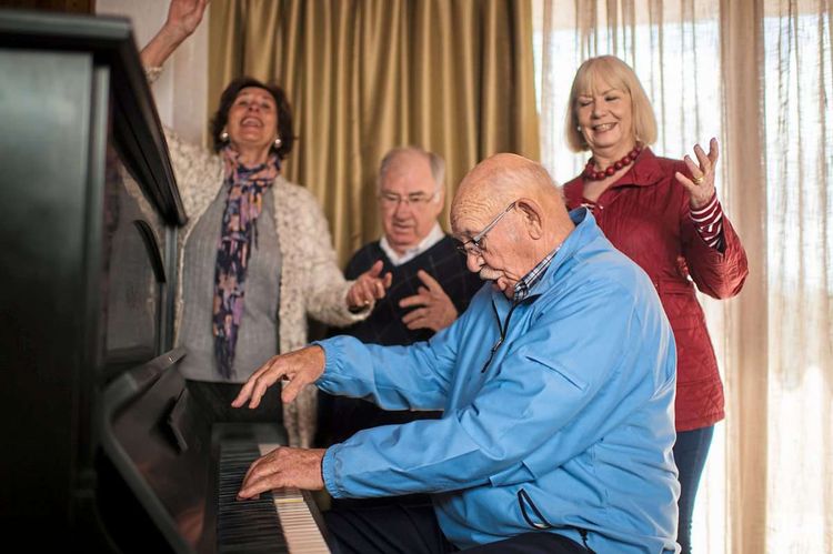 Eine Gruppe von Senioren und Seniorinnen an einem Klavier, die laut und ausdrucksstark zusammen singen und lachen