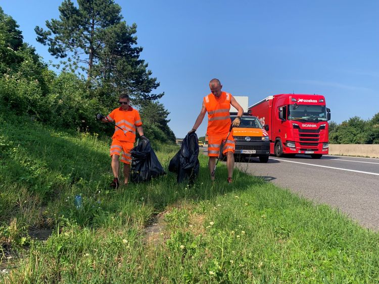 Männer sammeln auf der Autobahn Müll ein.