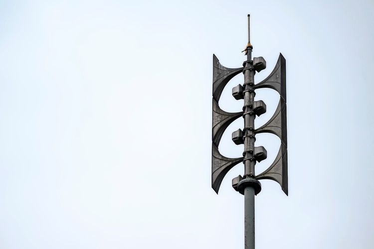 Eine moderne Sirene auf einem Mast vor klarem Himmel, aufgenommen während eines Zivilschutz-Probealarms in Wien, Österreich.