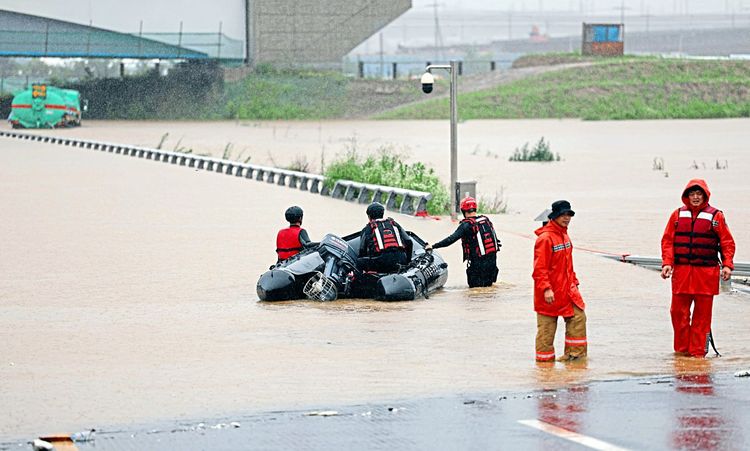 Die Einsatzkräfte suchen auf einer überfluteten Straße mit einem Boot nach Überlebenden.