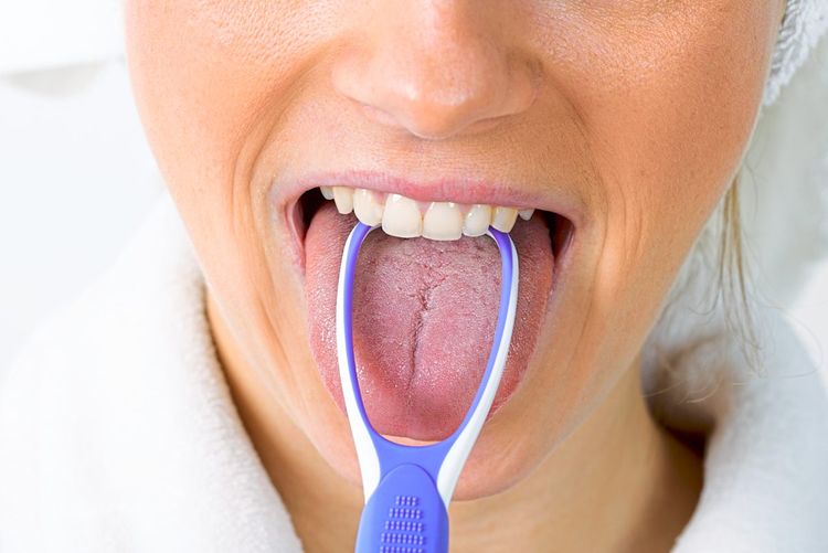 Eine Frau schabt sich mit einem Zungenschaber aus Kunststoff die Zunge ab.