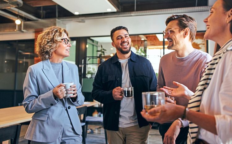 Gruppe von Arbeitskolleginnen und Kollegen, die gemeinsam einen Kaffee trinken und lachen