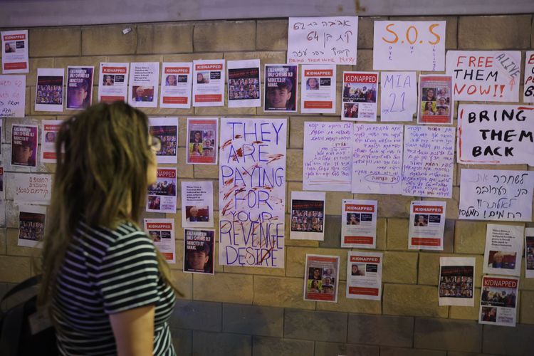 Eine junge Frau betrachtet Zettel mit Bildern von Entführten, die auf einer Mauer in Tel Aviv zu sehen sind.
