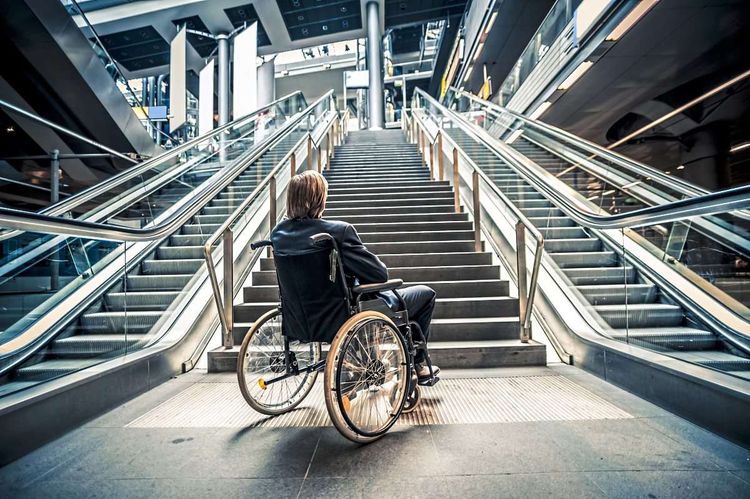Person in Rollstuhl vor Rolltreppe