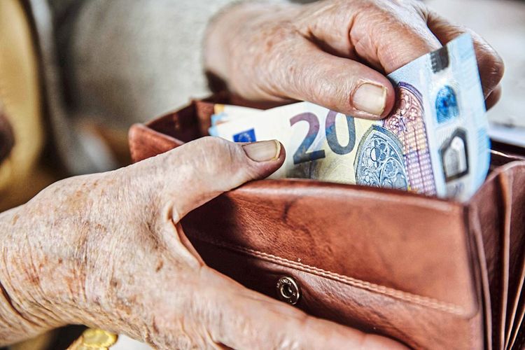 Hände einer älteren Frau, die einen 20-Euro-Schein aus ihrer Geldbörse zieht