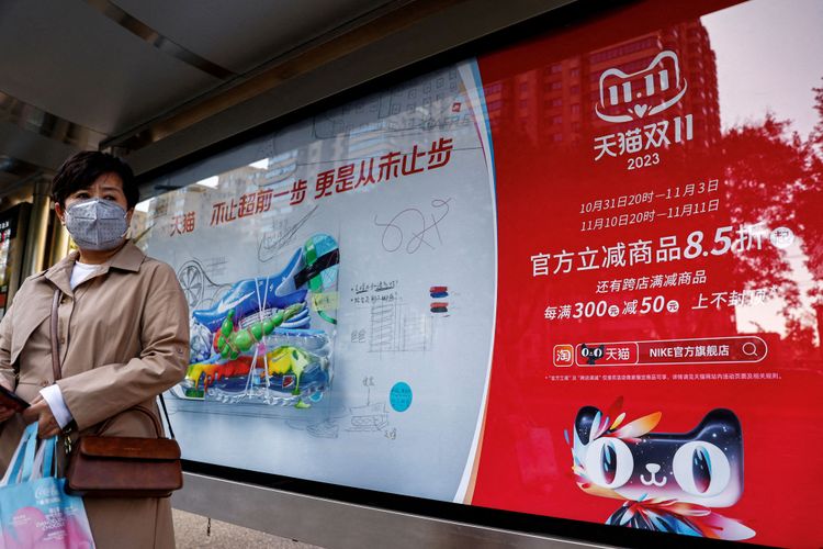 Eine Frau steht mit einem Einkaufssack vor einer Werbung des Online-Händlers Alibaba.