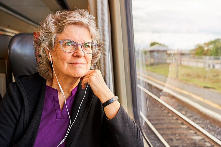 Eine Frau mit Kopfhörern schaut aus dem Zugfenster