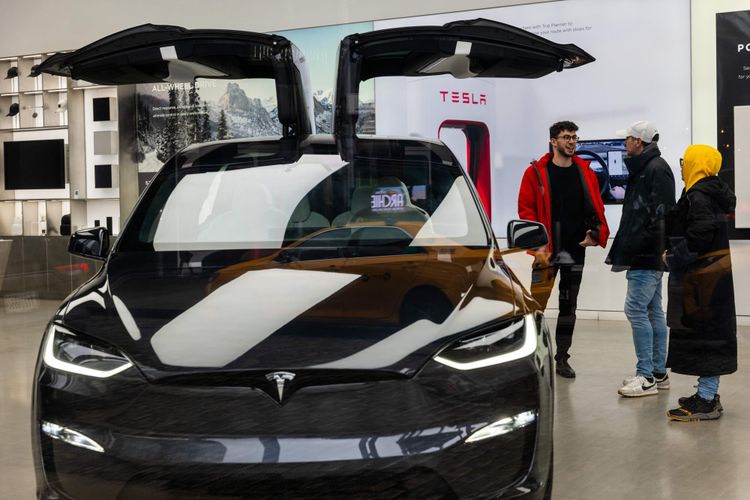 Ein Tesla vor einer Ladesäule, daneben stehen drei Personen.