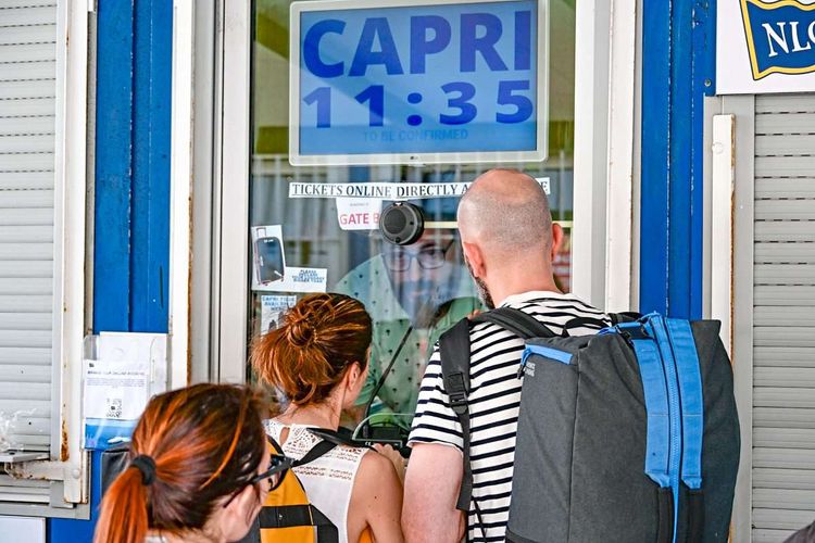 Schild mit Abfahrzeit für die Fähre nach Capri und Touristen vor einem Schalter