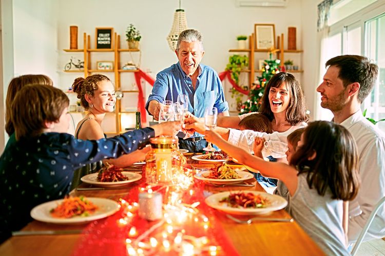Eine Familie sitzt am Tisch und feiert Weihnachten, sie heben gerade die Gläser