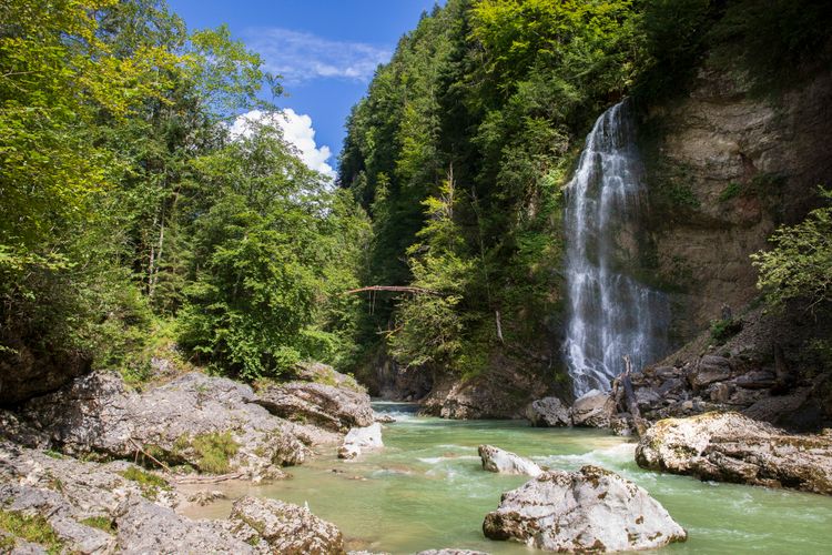 Ein Wasserfall stürzt von einem Felshang herab in einen Fluss.