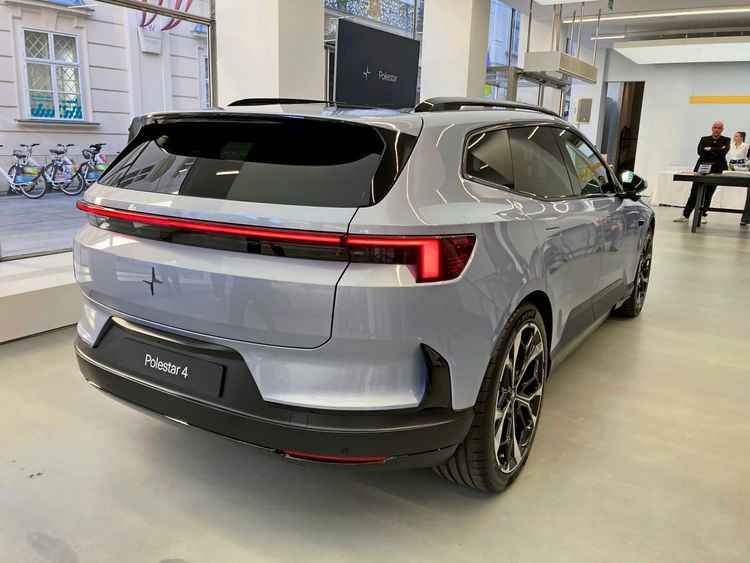 Rückansicht eines silbernen Polestar 4 SUV in einem modernen Ausstellungsraum mit großen Fenstern.