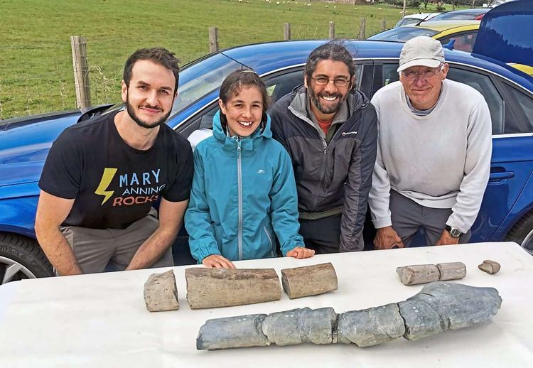 Ruby mit ihrem Vater und zwei Forschern vor einem Tisch mit Fossilien.
