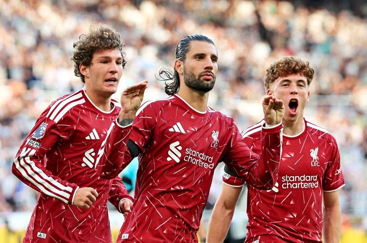 Drei Fußballspieler von Liverpool in roten Trikots feiern ein Tor während eines Spiels im St. James' Park in Newcastle. Einer der Spieler zeigt eine Geste mit den Fingern, während die anderen jubeln. Im Hintergrund sind unscharfe Zuschauer zu sehen.