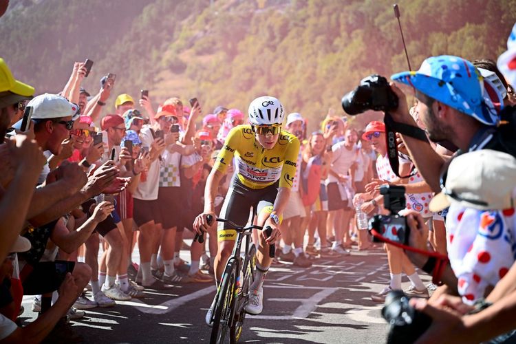 Ein Radfahrer im gelben Trikot fährt während einer Etappe der Tour de France 2026 eine Bergstraße hinauf, umgeben von jubelnden Zuschauern. Die Menschenmenge macht Fotos und feuert den Radfahrer an. Im Hintergrund sind bewaldete Berghänge erkennbar.