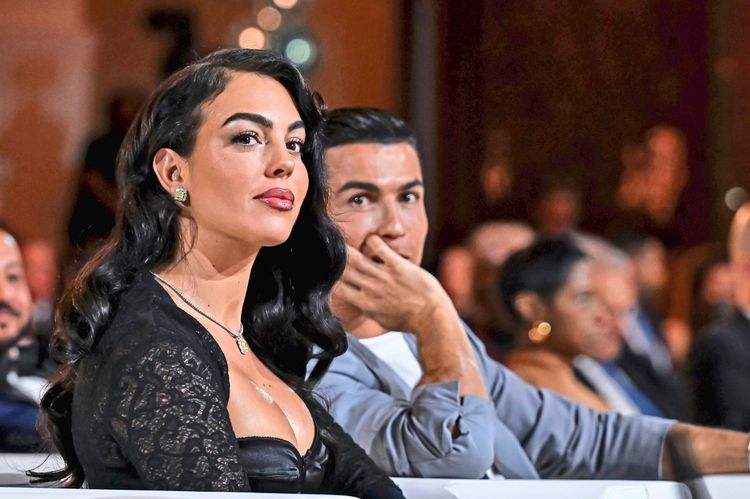 Eine Frau mit langen, dunklen Haaren und eleganter Kleidung sitzt neben einem Mann in einem grauen Anzug in einem Veranstaltungsraum. Beide blicken aufmerksam nach vorne. Im Hintergrund sind weitere Gäste unscharf erkennbar.
