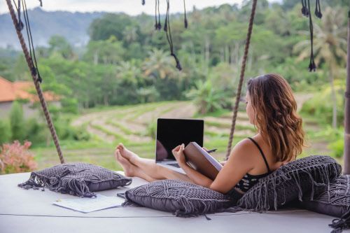 Frau sitzt mit Laptop auf Sofa mit Blick auf Reisterasse in Bali