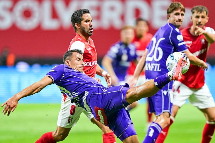 Ein Fußballspiel zwischen Sporting Braga und Austria Wien während der UEFA Conference League Play-offs. Ein Spieler im violetten Trikot versucht akrobatisch den Ball zu spielen, während ein Spieler im roten Trikot danebensteht. Im Hintergrund weitere Spieler und ein unscharfer Stadionhintergrund.